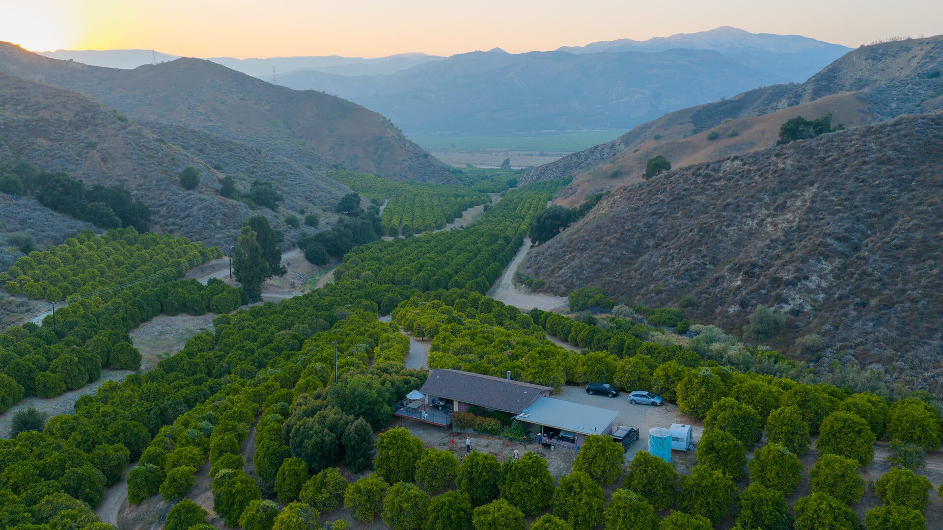 Aerial view of Paradise Ranch homestead at sunset, surrounded by orchards and mountains